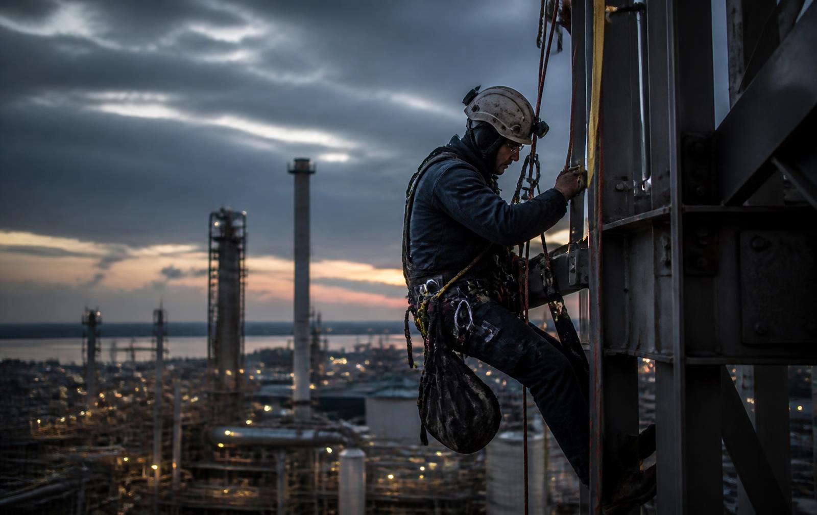 Rope access technician working at height on an industrial structure at dusk